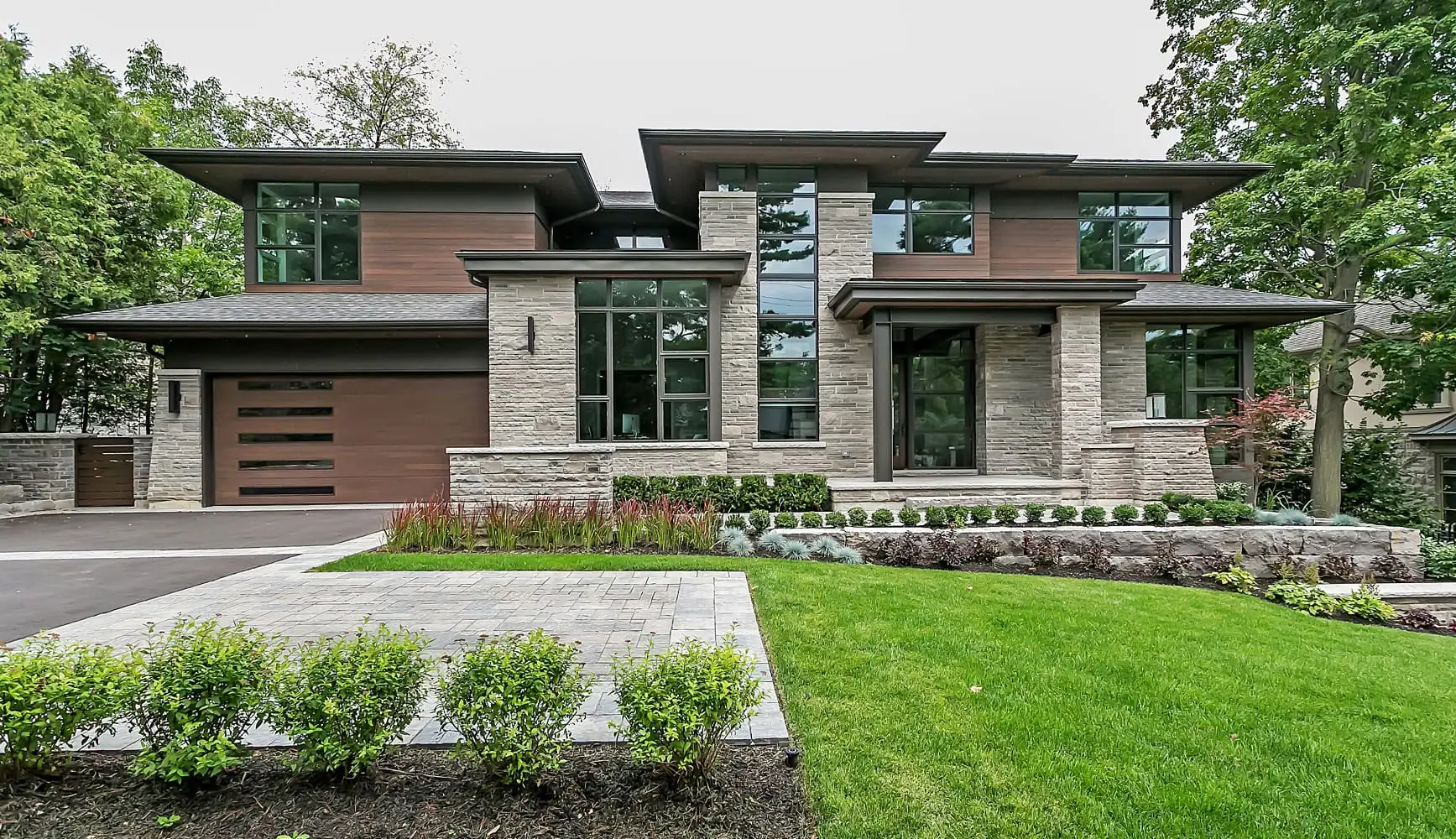 Modern stone house with an interlock front walkway, lawn and clean front planting beds